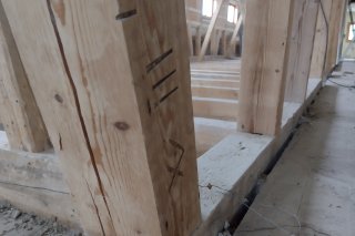 Holzpfosten in der Walserschanz Der Holzpfosten steht in einem Rohbau. Baustellenmaterial ist auf dem Boden verteilt. Handwerker arbeiten in der Nähe.