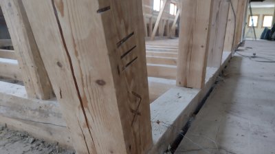 Der Holzpfosten steht in einem Rohbau. Baustellenmaterial ist auf dem Boden verteilt. Handwerker arbeiten in der Nähe.