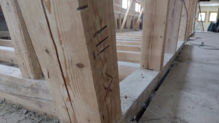 Holzpfosten in der Walserschanz Der Holzpfosten steht in einem Rohbau. Baustellenmaterial ist auf dem Boden verteilt. Handwerker arbeiten in der Nähe.