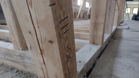 Holzpfosten in der Walserschanz Der Holzpfosten steht in einem Rohbau. Baustellenmaterial ist auf dem Boden verteilt. Handwerker arbeiten in der Nähe.