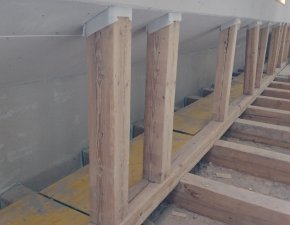 Holzstützen werden in einem Gebäude eingebaut. Es gibt auch eine Treppe und viele Werkzeuge auf dem Boden.