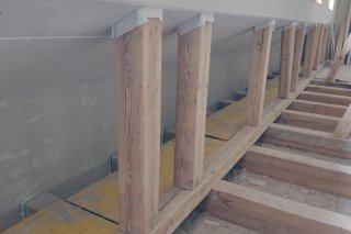 Holzstützen werden in einem Gebäude eingebaut. Es gibt auch eine Treppe und viele Werkzeuge auf dem Boden.