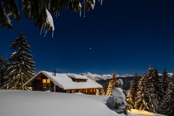WH Winter Außenansicht Markus Trienke Eine Außenansicht der verschneiten, beleuchteten Wannenkopfhütte bei Nacht.