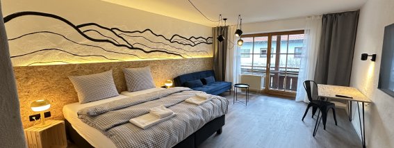 In einem Zimmer befinden sich ein großes Bett, ein Sofa und ein Schreibtisch. Es gibt viel Licht und eine schöne Aussicht.
