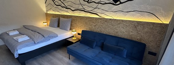 In einem Raum stehen ein Bett und ein Sofa. Die Wände haben eine einfache Dekoration und die Beleuchtung ist warm.