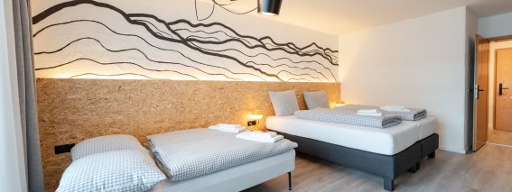 Das Zimmer hat zwei Einzelbetten und einen großen Fensterbereich. Die Wand hat ein einfaches Muster.