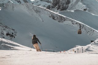 Ein Skifahrer fährt über den frischen Schnee in den Bergen. Die Gondel schwebt in der Ferne.