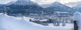 Schneebedeckte Berge umgeben ein ruhiges Tal, während Wolken über die winterliche Landschaft ziehen.