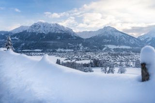 Schneebedeckte Berge umgeben ein ruhiges Tal, während Wolken über die winterliche Landschaft ziehen.