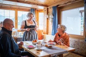 Gäste sitzen in einem Restaurant und genießen ihr Essen. Eine Bedienung bringt Speisen an den Tisch.