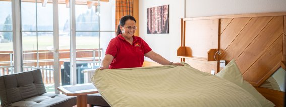 Eine Hotelangestellte schüttelt das Bett auf und bereitet alles für die Gäste vor.