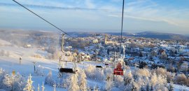 Die Szene zeigt den Sessellift am Adlerfelsen mit Blick auf eine verschneite Landschaft und die Stadt Eibenstock unter klarem Himmel.