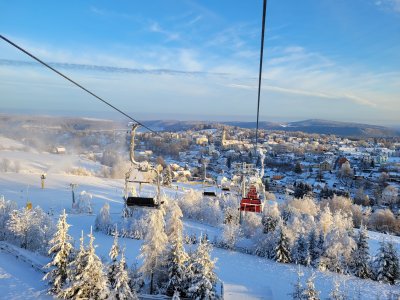 Die Szene zeigt den Sessellift am Adlerfelsen mit Blick auf eine verschneite Landschaft und die Stadt Eibenstock unter klarem Himmel.