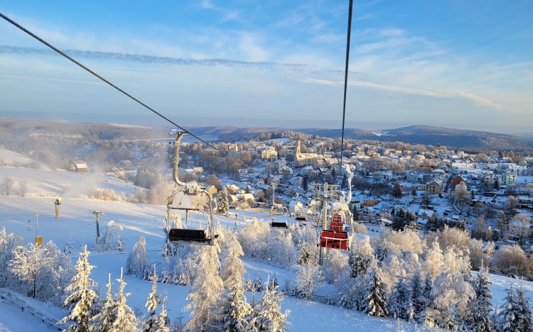 Die Szene zeigt den Sessellift am Adlerfelsen mit Blick auf eine verschneite Landschaft und die Stadt Eibenstock unter klarem Himmel.