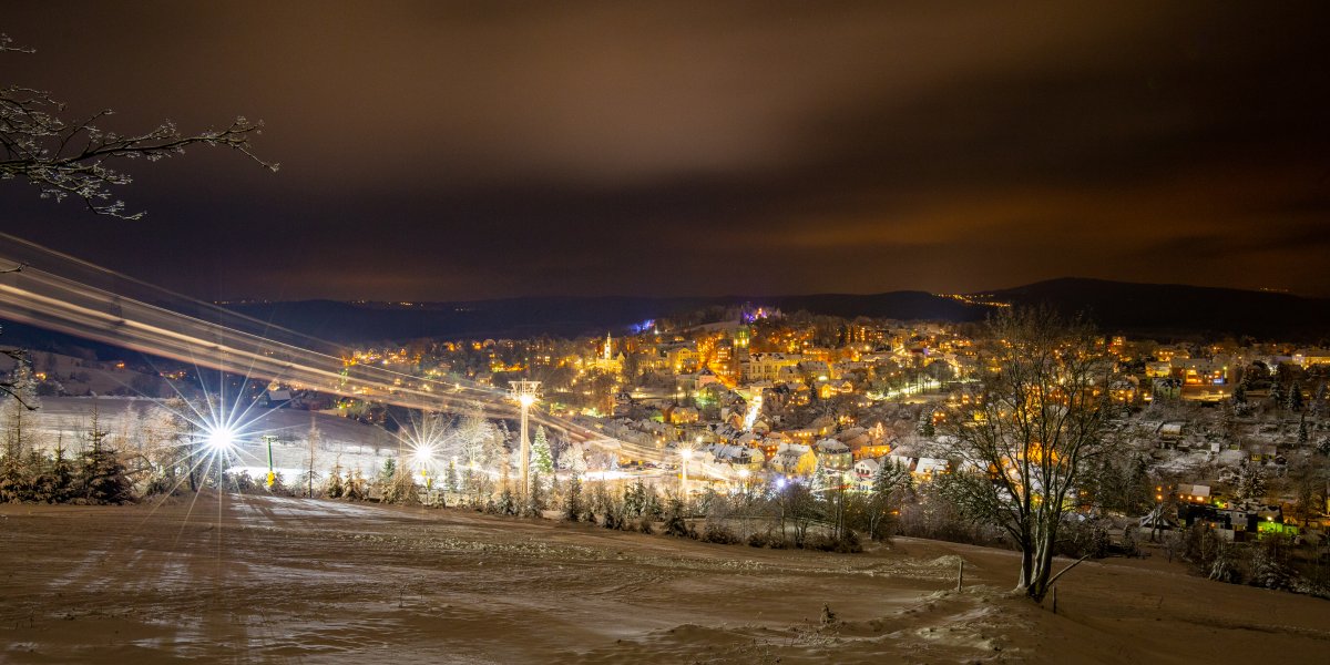 Die Stadt erstrahlt nachts in warmem Licht, während Schnee die Landschaft bedeckt und die Stille des Winters verleiht.