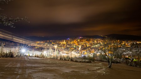 Die Stadt erstrahlt nachts in warmem Licht, während Schnee die Landschaft bedeckt und die Stille des Winters verleiht.
