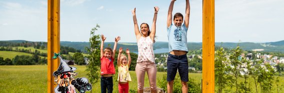Eine Familie posiert fröhlich vor einem großen Bilderrahmen in der Natur. Es ist ein schöner Sonnentag bei Wurzelrudi im Sommer.