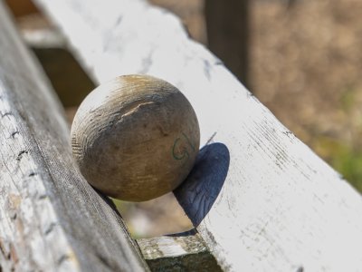 Ein Holzball liegt auf einer Bank und rollt. Es ist ein sonniger Tag und die Umgebung ist ruhig und grün.