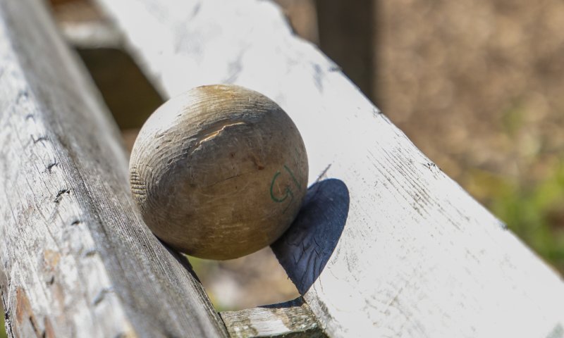 Ein Holzball liegt auf einer Bank und rollt. Es ist ein sonniger Tag und die Umgebung ist ruhig und grün.