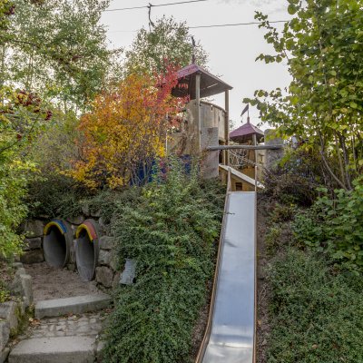 Ein Spielplatz hat eine Rutsche und viele Pflanzen rundum. Kinder können hier spielen und die Natur genießen.