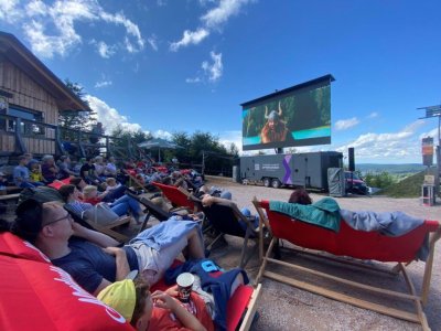 Menschen sitzen auf Liegestühlen und sehen einen Film im Freien. Das Wetter ist sonnig und die Stimmung ist entspannt. Moviequidi-Eibenstock