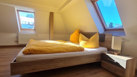 In diesem hellen Schlafzimmer stehen ein großes Bett und zwei gelbe Kissen. Der Raum hat eine schöne Dachfensteransicht.