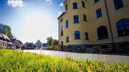 Ein modernes Gebäude steht an der Straße. Die Sonne scheint. Gras wächst auf dem Bürgersteig. Es ist ein klarer Tag.