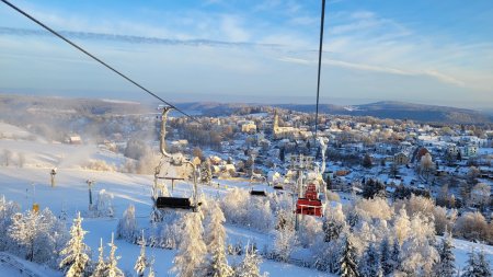 Die Skilifte stehen hoch über einer verschneiten Stadt. Menschen fahren auf den liften und genießen den Wintertag.