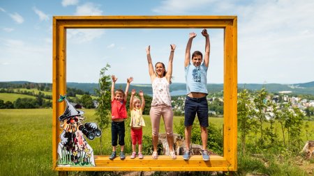 Eine Familie mit drei Kindern steht im Freien und hebt die Arme. Sie lächeln in die Kamera und genießen die Zeit zusammen.