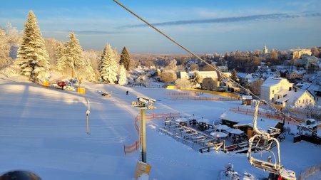 Ein Skilift steht in einer verschneiten Landschaft. Bäume und Hügel sind mit Schnee bedeckt. Der Himmel ist blau.