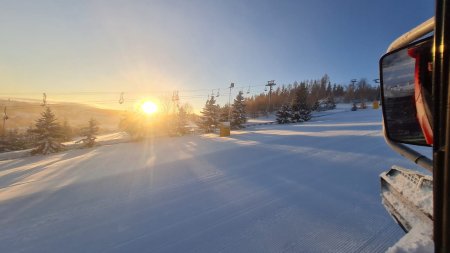 Die Sonne steht auf und beleuchtet die Schneepiste. Skilifte sind in der Nähe und die Landschaft ist winterlich.